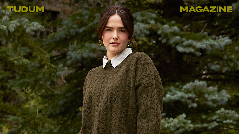Zoey Deutch stands against a backdrop of trees