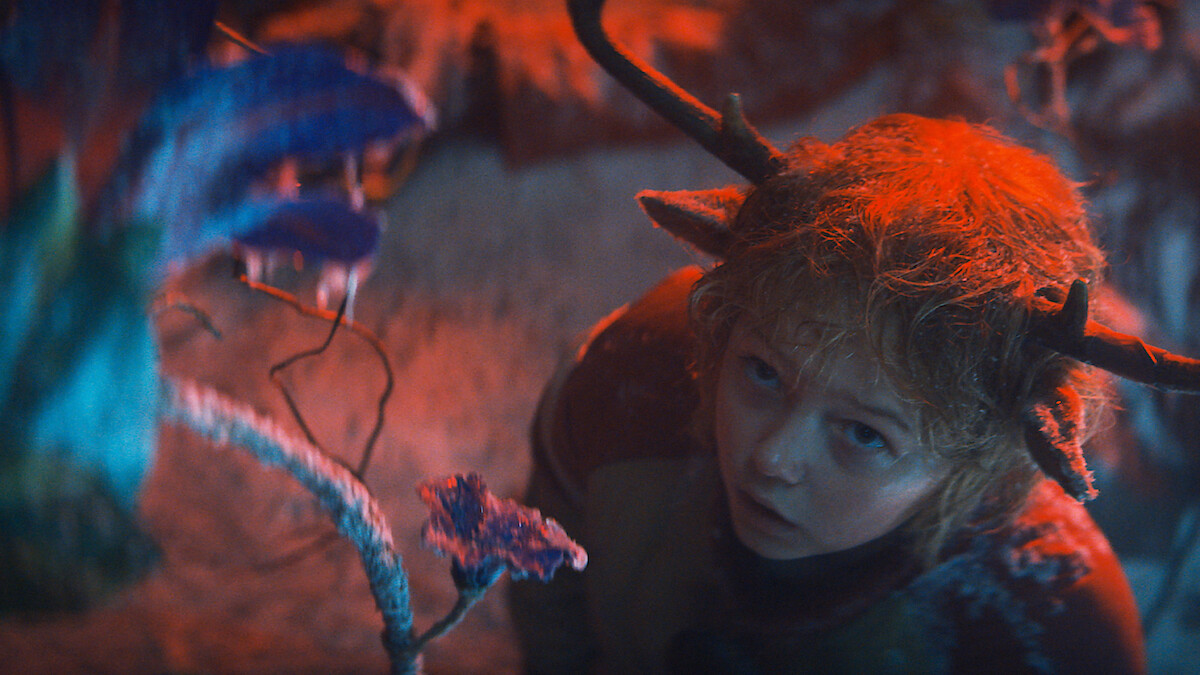 Christian Convery as Gus looks at a purple flower while shrouded in red light in Season 3 of 'Sweet Tooth'