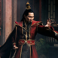 A man in ornate red and gold robes with a flame-shaped crown stands in a traditional Asian architectural setting, striking a dynamic pose with an intense expression.