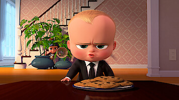 Animated baby in a suit sits at a table with a plate of cookies, looking serious, while a child hides behind potted plants in a cozy home with staircase and wallpaper in the background.