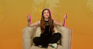 Lucy Paez snaps her hands while sitting casually on an oversize chair.