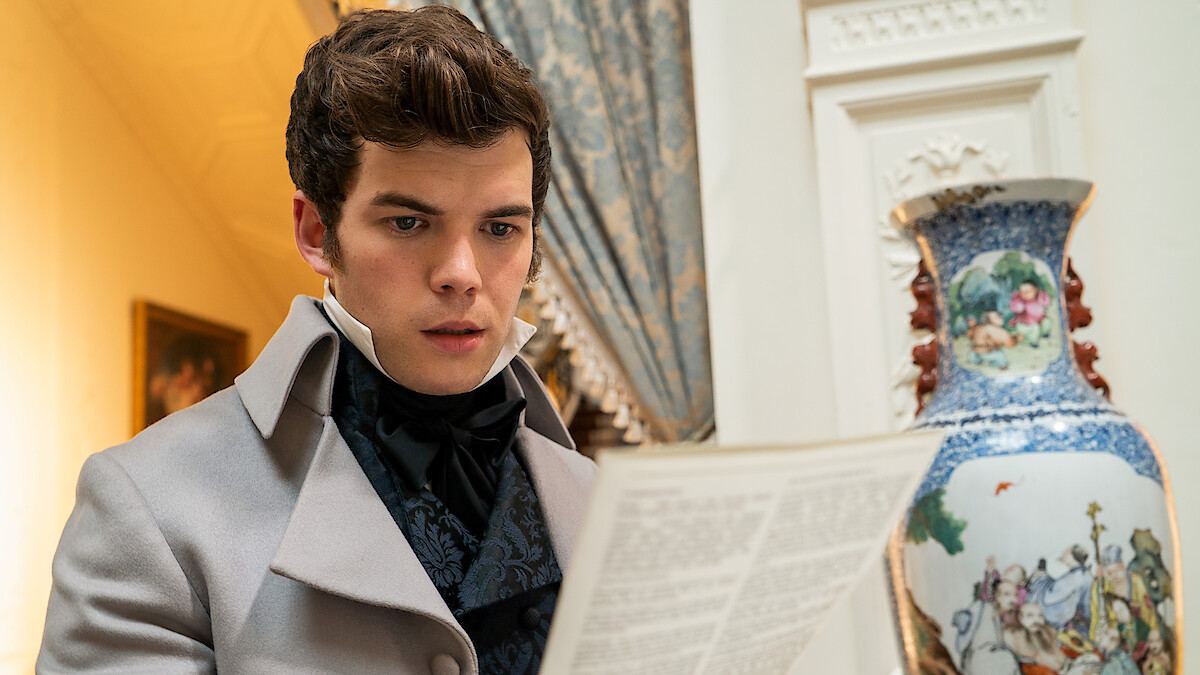A young man in period costume reads a letter or paper indoors, standing near a large ornate vase with a decorative pattern in an elegant room with classic furnishings and drapery.