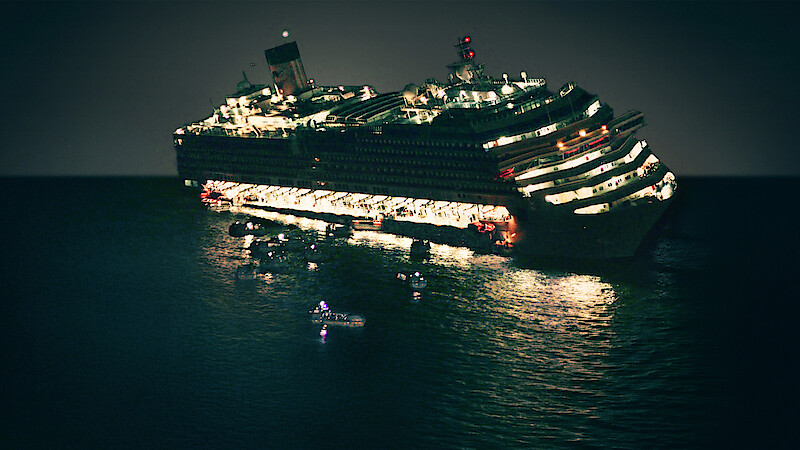 Large cruise ship tilting at night on the sea, illuminated with lifeboats and rescue boats in the water nearby, suggesting an emergency or evacuation situation.