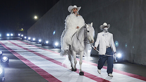Beyoncé wearing a white fur coat and white cowgirl hat, sitting on a white horse.