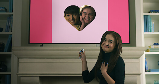 Anna Cathcart smiles in front of a screen with a photo of Kitty and Dae in a heart