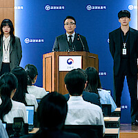 A group of four people face a group of reporters at a press conference.