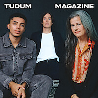 From left to right, Jay Lycurgo, Cillian Murphy, and Tracey Ullman sit around a table against a dark slate grey background.