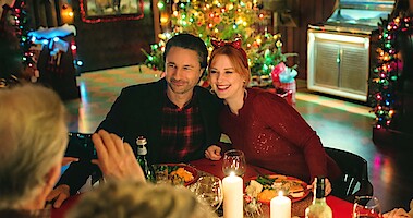 Martin Henderson as Jack Sheridan and Alexandra Breckenridge as Mel Monroe smile at a dinner table with Christmas decorations in the background in Season 5 of 'Virgin River.'