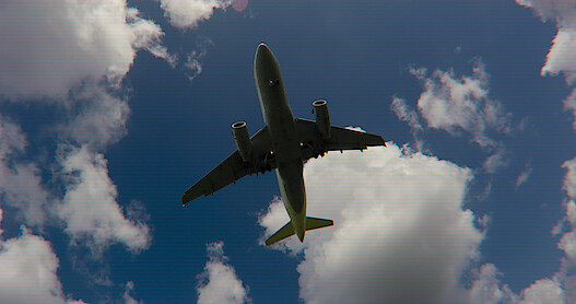 A jet flies through the air with blue sky and clouds.