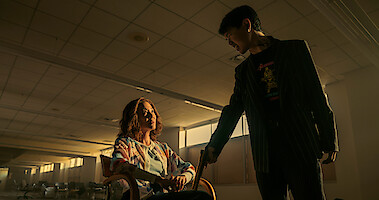 Michelle Yeoh as Mama Sun sitting in an empty room with an armed interrogator in 'The Brothers Sun.'