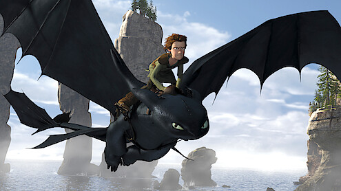 Animated boy riding a black dragon flying over a misty coastal landscape with tall rock formations and a blue sky with scattered clouds in the background.