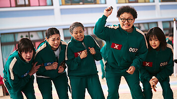 Squid Game players in teal tracksuits compete in a game. 