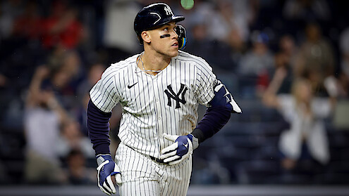 New York Yankees baseball player in pinstripe uniform runs on field during a night game; blurred crowd in the background creates an energetic, competitive atmosphere.