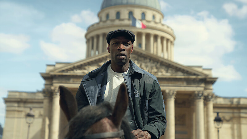 Man riding a horse in front of a historic building with a dome and French flag, under a blue sky with scattered clouds, urban setting.