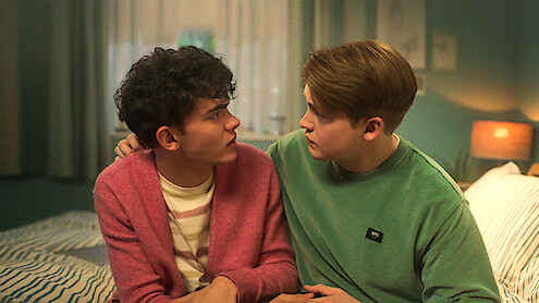 Joe Locke as Charle and Kit Connor as Nick sit on a bed together looking into each other's eyes in Season 3 of 'Heartstopper'