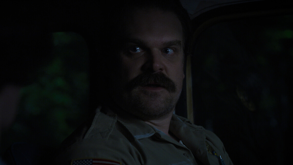 David Harbour as Hopper sitting in a dark truck in 'Stranger Things' Season 3.