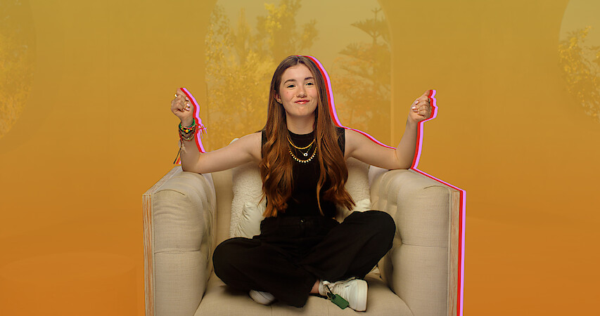 Lucy Paez snaps her hands while sitting casually on an oversize chair.