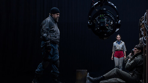 Cena tensa em um set de filmagem com três atores e um grande equipamento de câmera.