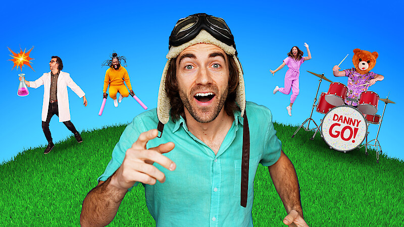 Danny GO! in an aviator hat smiling on grass under blue sky, with scientist holding beaker, person with pink bats, woman jumping, and bear costume playing drums labeled "Danny Go!" in colorful, playful setting.
