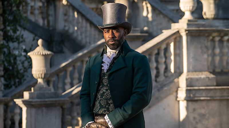 A man in Victorian-era formal attire and top hat stands outside in front of elegant stone steps and balustrades, with classic architecture in the background.