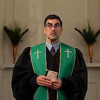A pastor standing in front of a cross on a wall