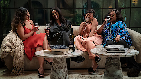 Four women sit on a beige couch in an elegant living room, laughing and enjoying glasses of wine, with books, throw blanket, and a wine bottle on marble coffee tables, creating a cozy, relaxed, and joyful atmosphere.