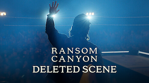 Thomas Rhett stands on stage in silhouette, facing bright spotlights with one hand raised. Smoky blue lighting fills the scene, the audience is barely visible in the background, and a text overlay reads: "Ransom Canyon Deleted Scene."