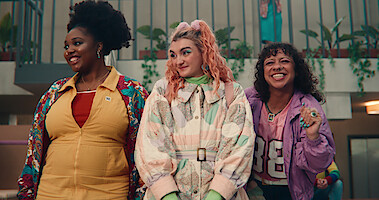Alexandra James as Aisha, Anthony Lexa as Abbi, and Felix Mufti as Roman stand together smiling at school in Season 4 of 'Sex Education.'