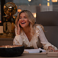 Kate Hudson as Isla Gordon sits at a desk smiling surrounded by basketball trophies in season 1 of 'Running Point'