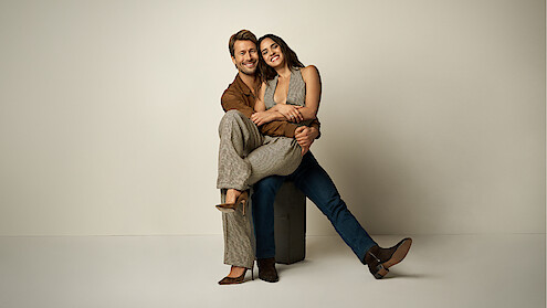 Adria Arjona sits on a Glen Powell's lap.