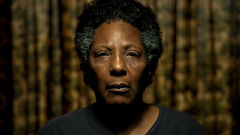 Imagem mostra uma mulher negra idosa em close, com os cabelos parcialmente brancos à mostra e a expressão séria