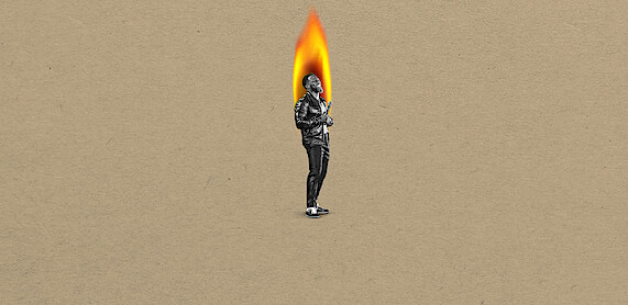 Kevin Hart in black-and-white stands on a tan background, with their head replaced by a large bright flame, suggesting a surreal or artistic concept.
