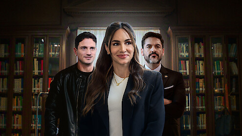 Three professionally dressed people stand in front of bookshelves in a library, with one woman in the center smiling confidently and two men flanking her, one in a black jacket and the other in a suit.