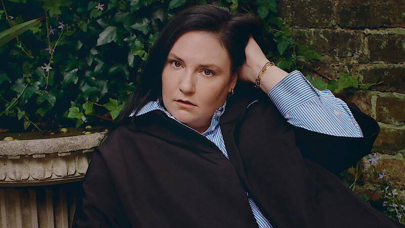 Headshot of Lena Dunham against a brick wall.