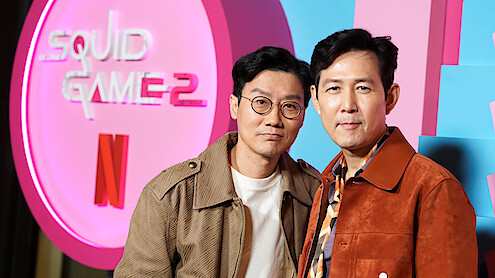 Hwang Dong-hyuk and Lee Jung-jae stand in front of a 'Squid Game 2' logo at Netflix's 'Squid Game' Fall Showcase at TUDUM Theater.