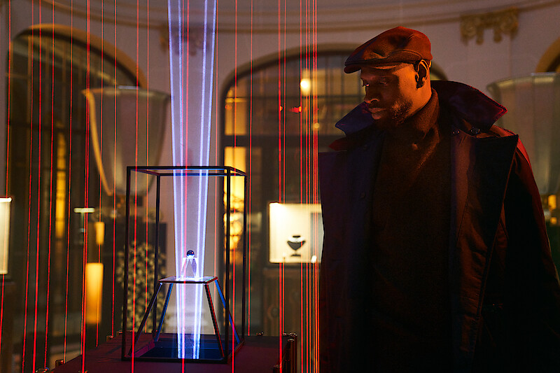 Omar Sy as Assane Diop stares at a mysterious object surrounded in red lasers in Season 3 of 'Lupin.' 