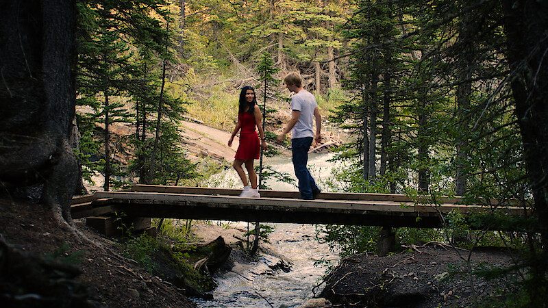 Jackie and Cole walk across a bridge in a forest