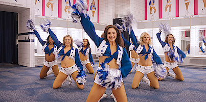 Formation of cheerleaders in DCC uniform practice inside fitting room in triangle formation while raising their right hands with pom poms up in the air confidently.