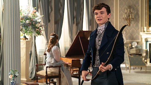 Will Tilston as Gregory Bridgerton in Regency attire holding a bow in an elegant, classic drawing room.