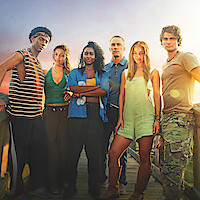 Six young adults stand on a dock at sunset, dressed in casual summer clothes, looking at the camera with serious expressions. The sky is colorful, creating a warm and adventurous atmosphere.
