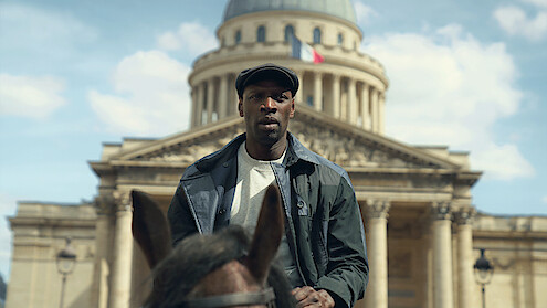 Man riding a horse in front of a historic building with a dome and French flag, under a blue sky with scattered clouds, urban setting.
