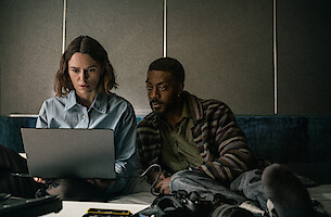 Keira Knightley and David Ajala look at a laptop together.