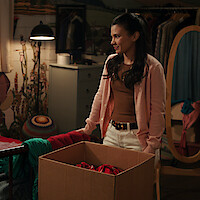 Nikki Rodriguez as Jackie sorting through clothes in a bedroom in 'My Life with the Walter Boys' Season 2.