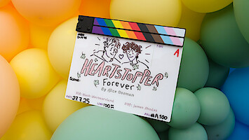 A film clapperboard with "Heartstopper Forever" illustrated, featuring two drawn characters and surrounded by colorful pastel balloons in the background.