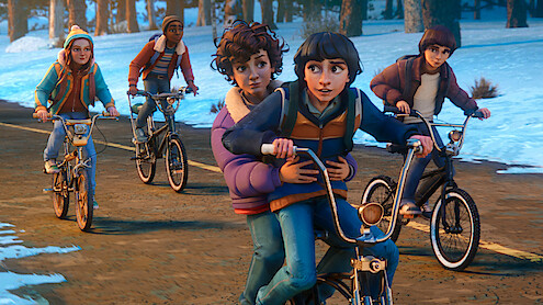 Five animated children riding bicycles together on a road bordered by snow and trees, wearing winter clothes and looking cheerful, suggesting friendship and adventure in a cold outdoor environment.