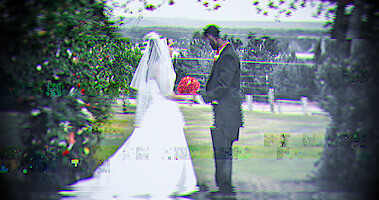 In an archival photo from the series 'Worst Ex Ever,' a bride and groom outside on their wedding day hold hands as if at an alter while standing on grass in between tall shrubs.