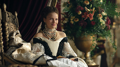 Uma mulher veste trajes de realeza e se senta em um trono na série 'The Empress'