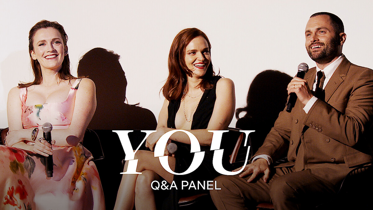 From left to right, Charlotte Ritchie, Madeline Brewer, and Penn Badgley sitting on a panel, each holding a microphone and smiling. They are dressed in formal attire, with the text "YOU Q&A PANEL" overlaid on the image.