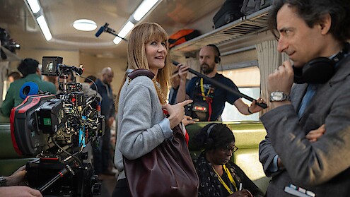 Film crew and actors on a busy train set, surrounded by cameras and equipment, with a focused yet lively atmosphere, suggesting a behind-the-scenes look at a movie production.