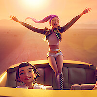 Two animated young women in a convertible at sunset, one standing joyfully with arms outstretched, the other smiling while seated, driving through a desert landscape with warm, golden sunlight illuminating the scene.